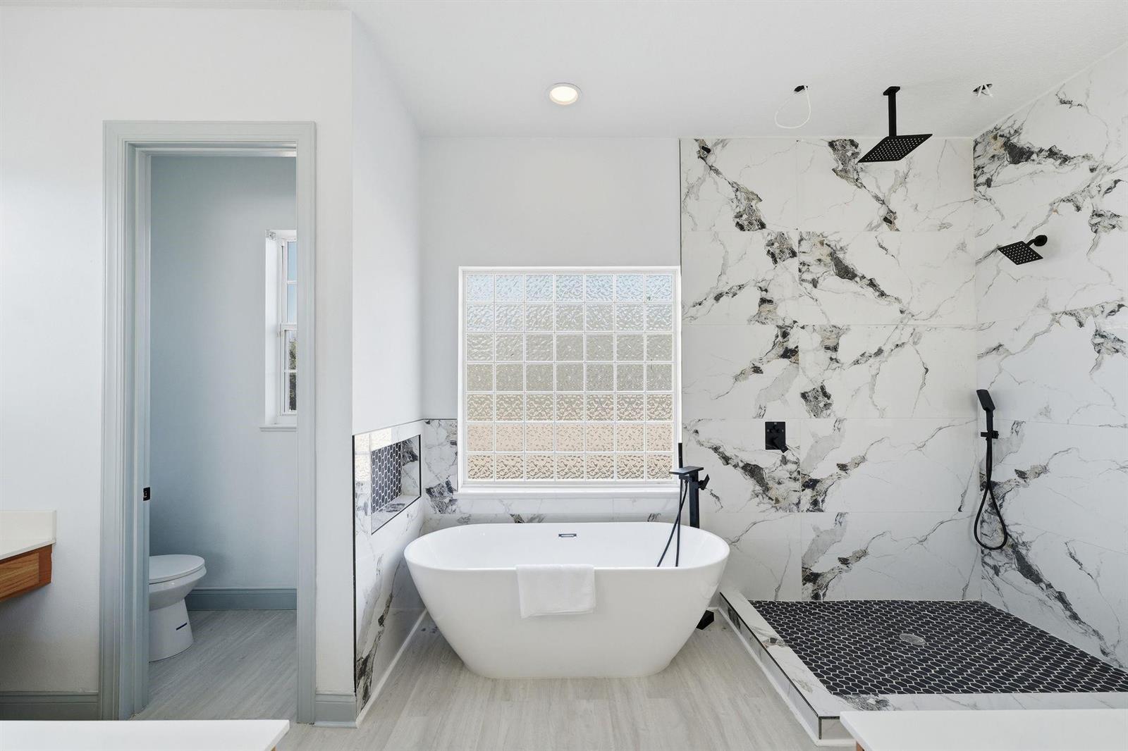 A modern bathroom features a freestanding tub, a walk-in shower with marble tile, and glass blocks — 4873 NE 64th Avenue, FL 34488, FL