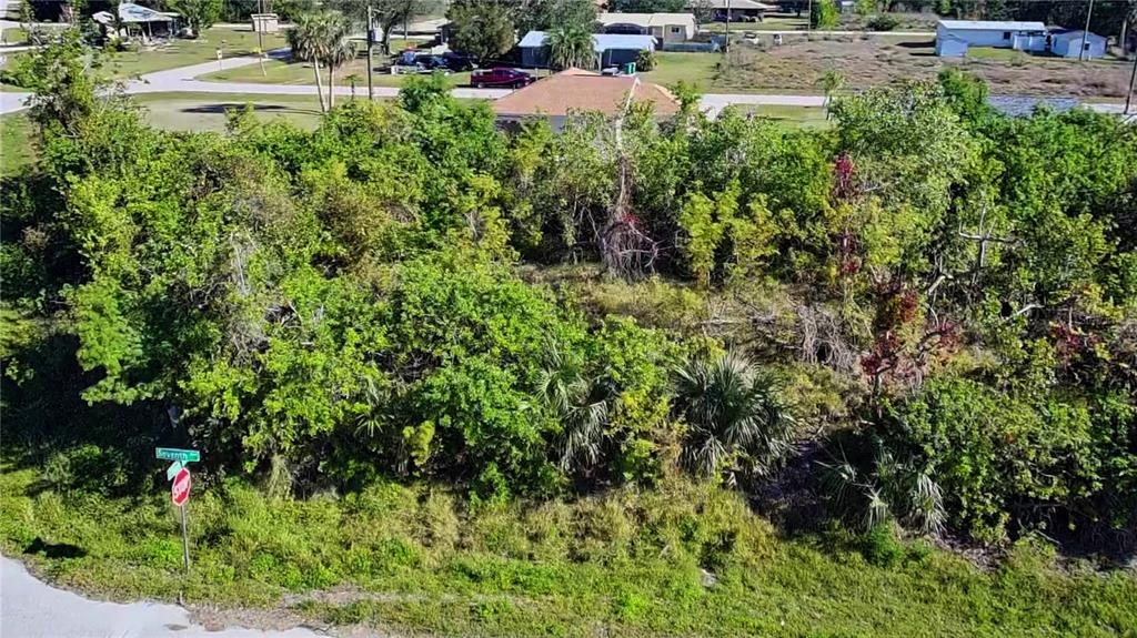 An aerial view shows a densely wooded, undeveloped residential lot at a street corner — 11272 7TH AVENUE, PUNTA GORDA, FL