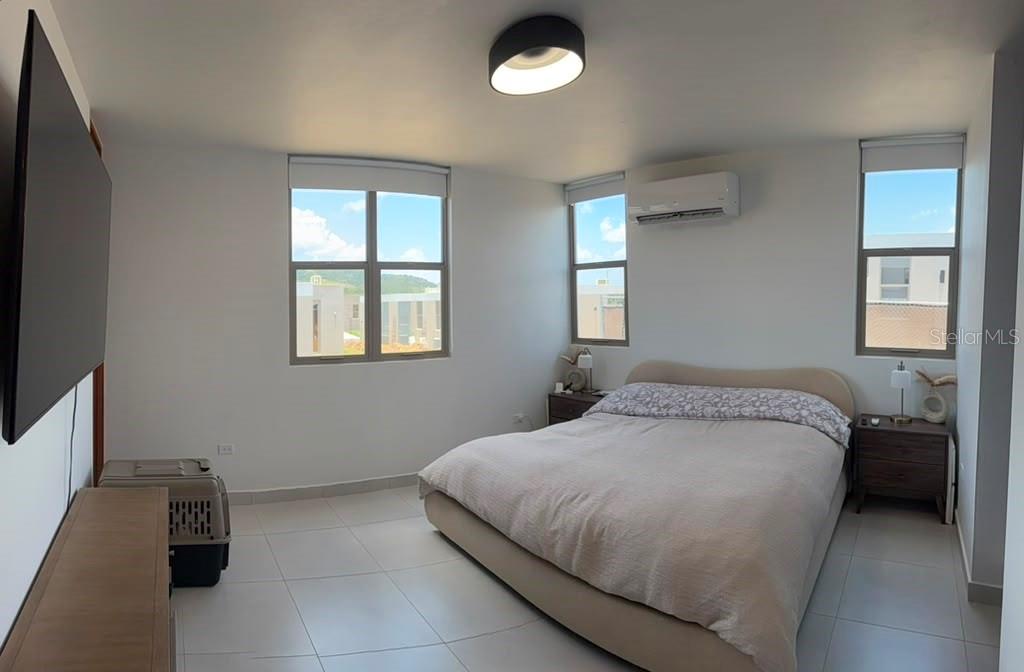 A bedroom features a bed, two nightstands, a wall-mounted television, and tile flooring — 110 St. RIVER VIEW CIUDAD JARDIN, GURABO, PR