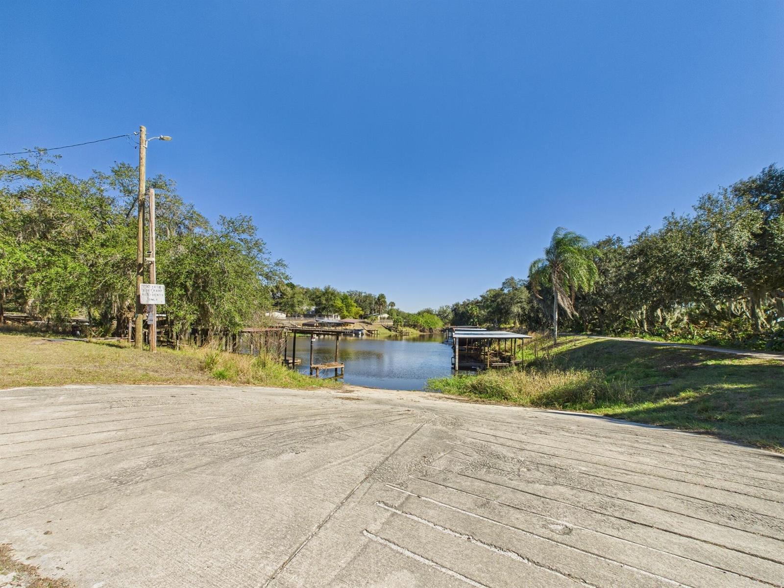 A concrete boat ramp leads down to a calm lake with several covered boat slips — 56 Basin Street, FL 33857, FL