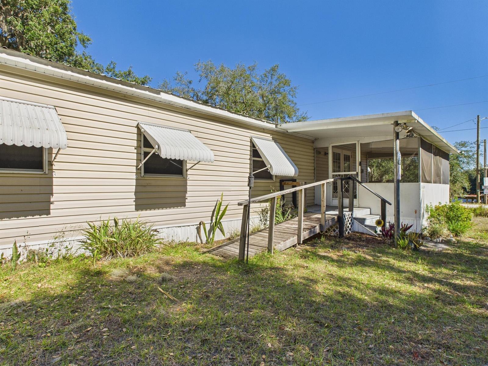 The exterior of a tan mobile home features a wooden wheelchair ramp and screened porch — 56 Basin Street, FL 33857, FL