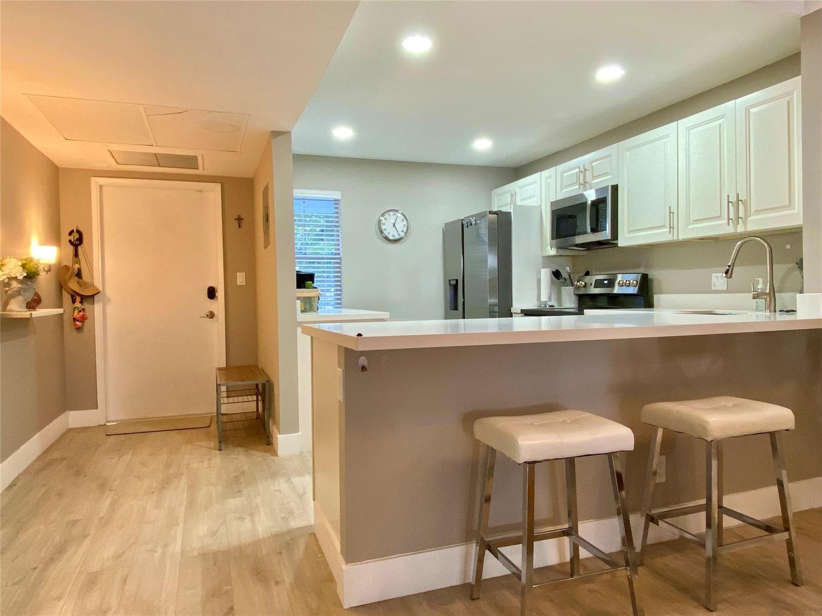 A kitchen features white cabinets, stainless steel appliances, a breakfast bar, and two stools — 3010 N Course Drive # 209, Pompano Beach FL 33069, POMPANO BEACH, FL