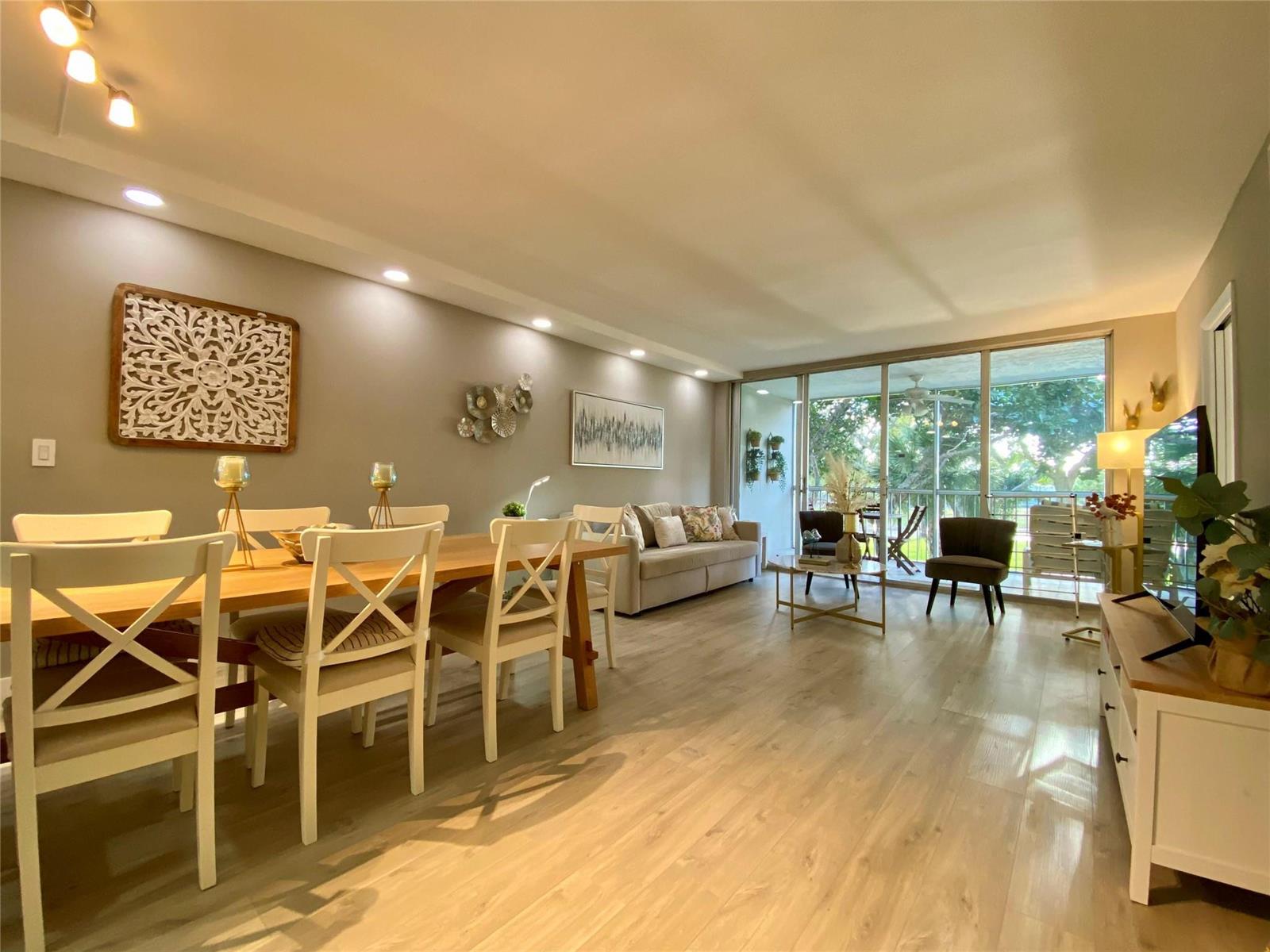 A bright, open-concept living and dining area features light wood flooring and sliding glass doors — 3010 N Course Drive # 209, Pompano Beach FL 33069, POMPANO BEACH, FL