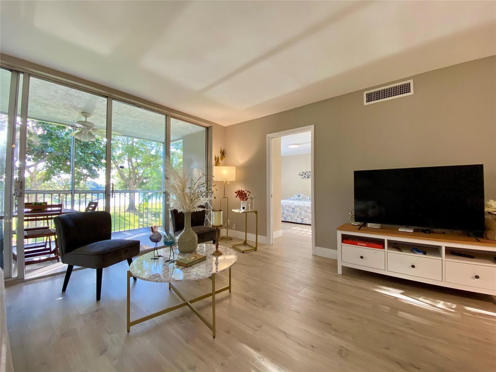 A living room features light wood floors, a marble coffee table, and a sliding glass door — 3010 N Course Drive # 209, Pompano Beach FL 33069, POMPANO BEACH, FL