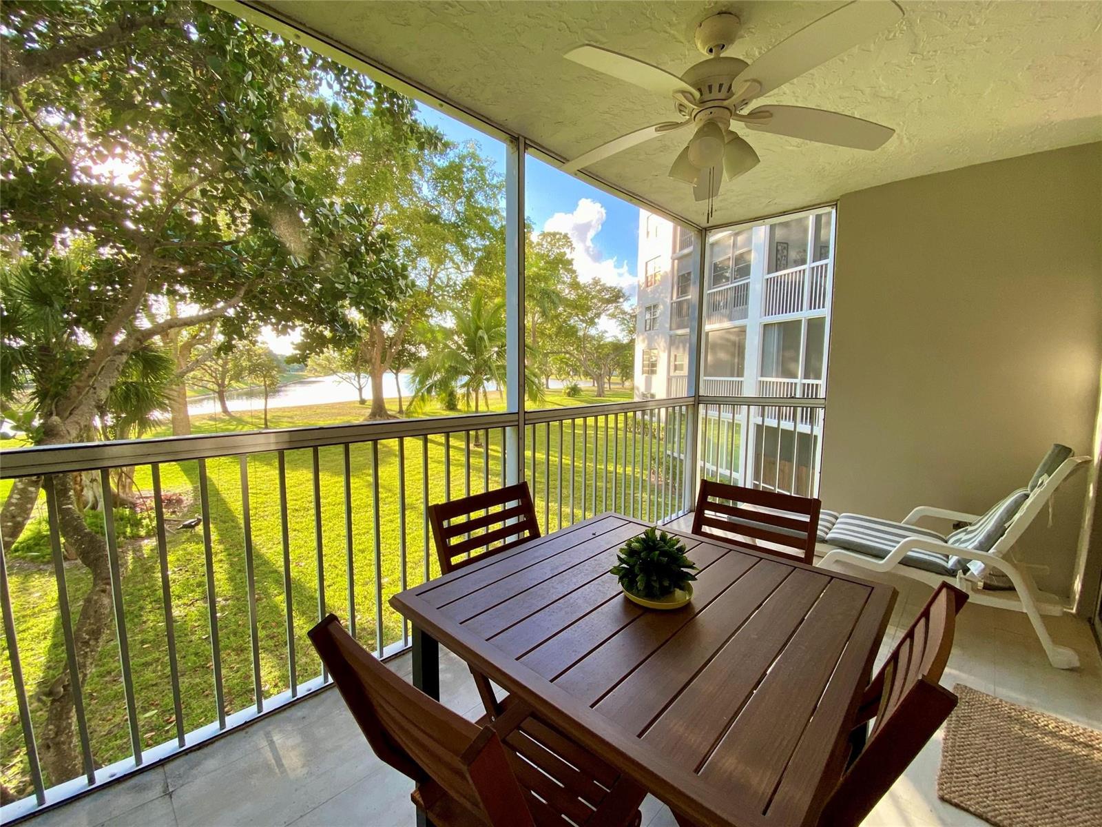 A screened-in balcony features a wooden dining set, a ceiling fan, and a lake view — 3010 N Course Drive # 209, Pompano Beach FL 33069, POMPANO BEACH, FL