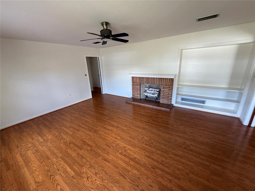 An empty living room features hardwood floors, a brick fireplace, and built-in shelving — 1485 DAVIS AVENUE, BARTOW, FL