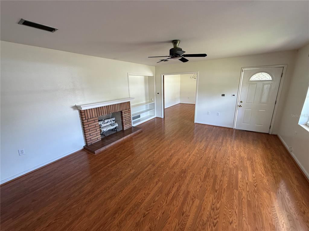 A living room features a brick fireplace, built-in shelving, hardwood floors, and a ceiling fan — 1485 DAVIS AVENUE, BARTOW, FL