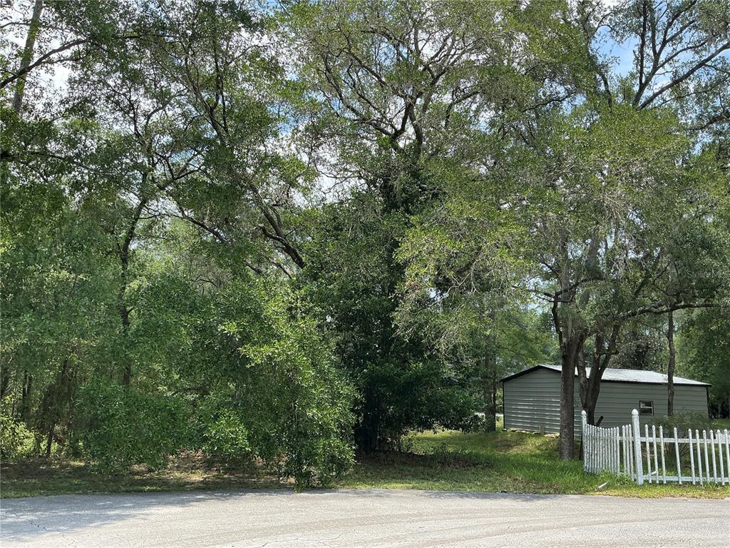 A wooded residential lot features a small metal shed and a white picket fence — SW 90TH PLACE, DUNNELLON, FL