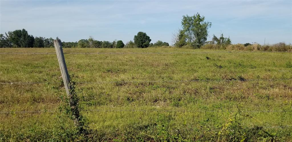 A wooden fence post stands in the foreground of a large, grassy, open field — HAYMAN ROAD, BROOKSVILLE, FL