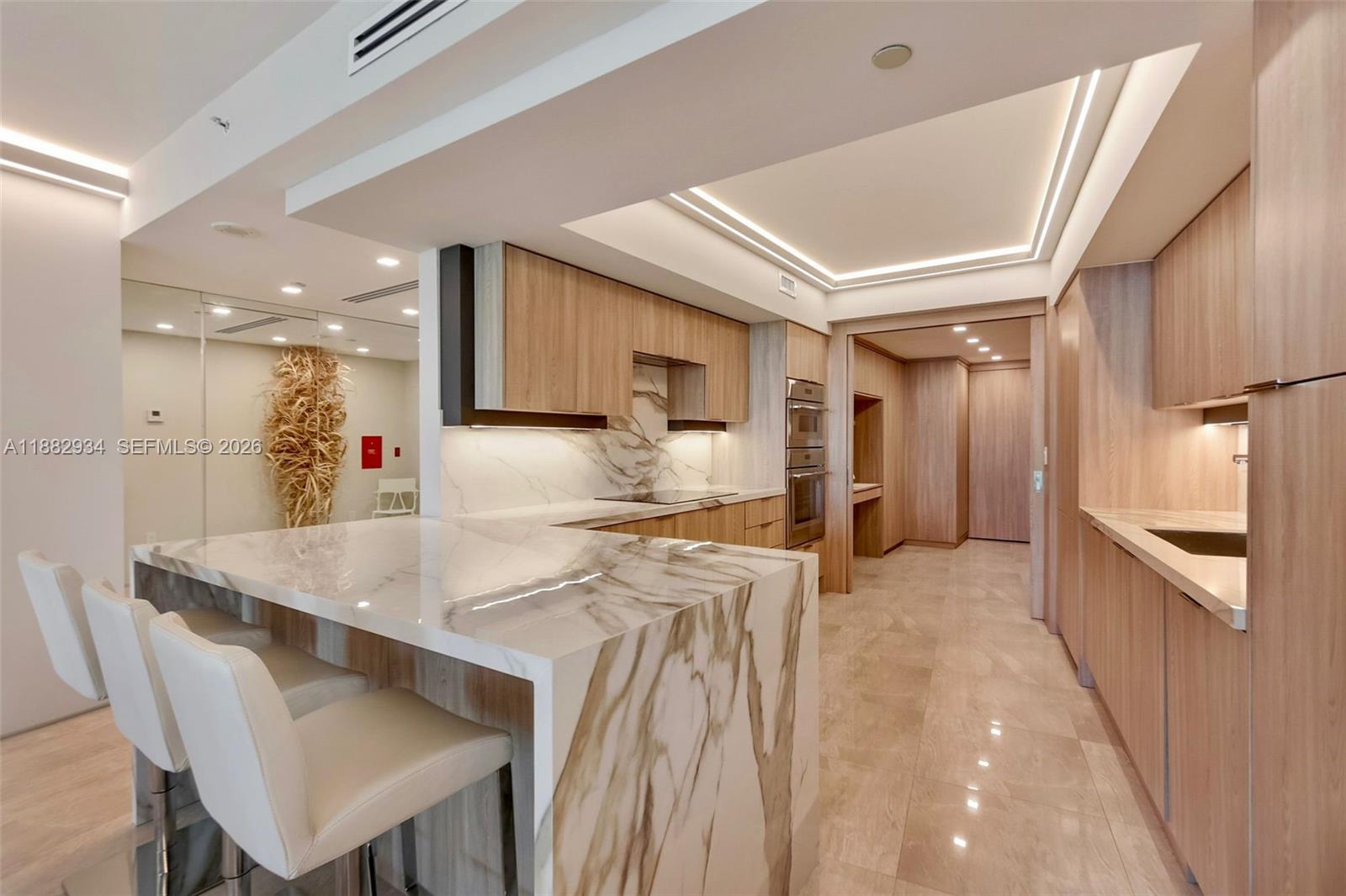 A modern kitchen features a marble waterfall island with three white bar stools — 1455 Ocean Dr # 811, Miami Beach FL 33139, MIAMI BEACH, FL