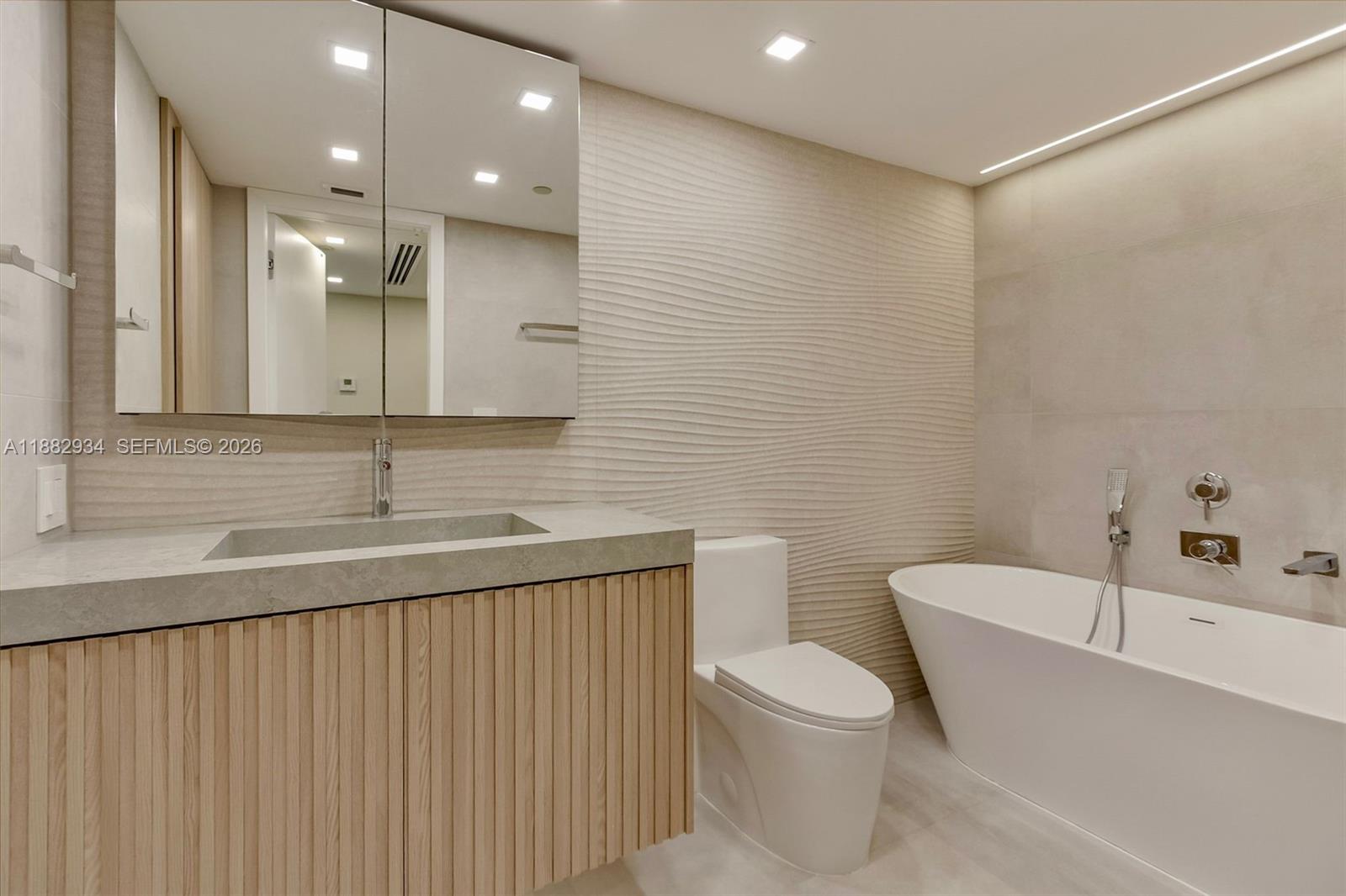 A modern kitchen features a marble waterfall island, light wood cabinetry, and recessed lighting — 1455 Ocean Dr # 811, Miami Beach FL 33139, MIAMI BEACH, FL