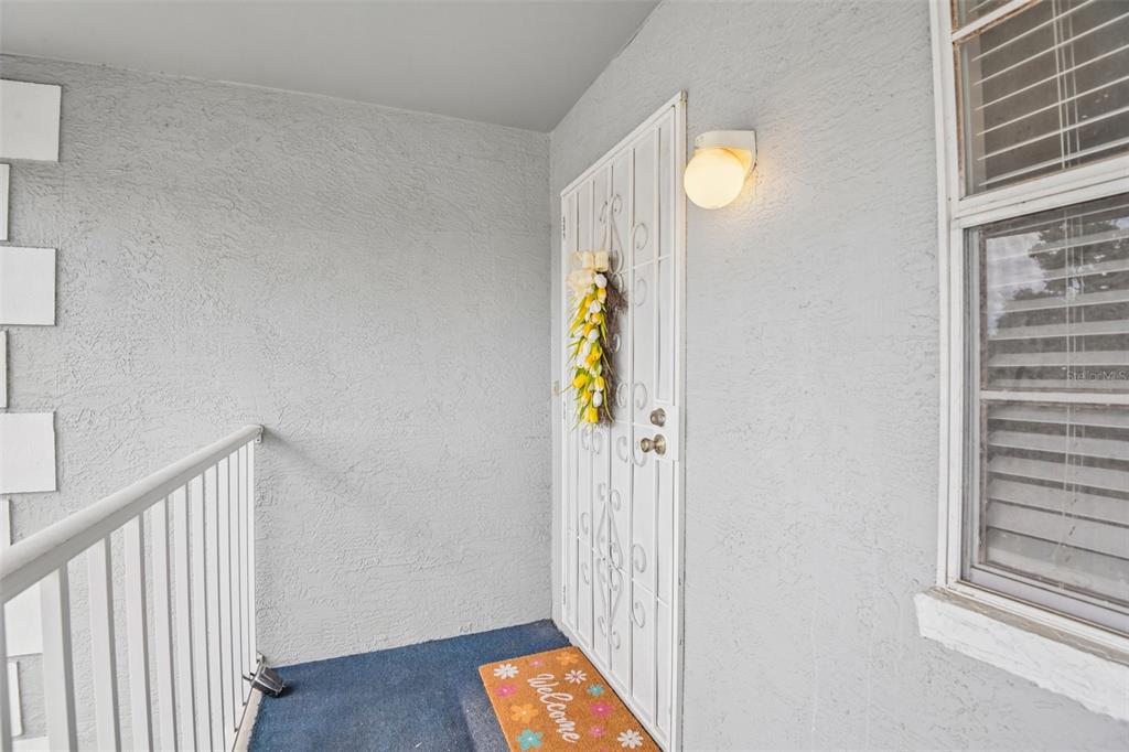 A white security door with a floral wreath sits on a covered exterior porch — 7713 HILLSIDE COURT UNIT 204, HUDSON, FL