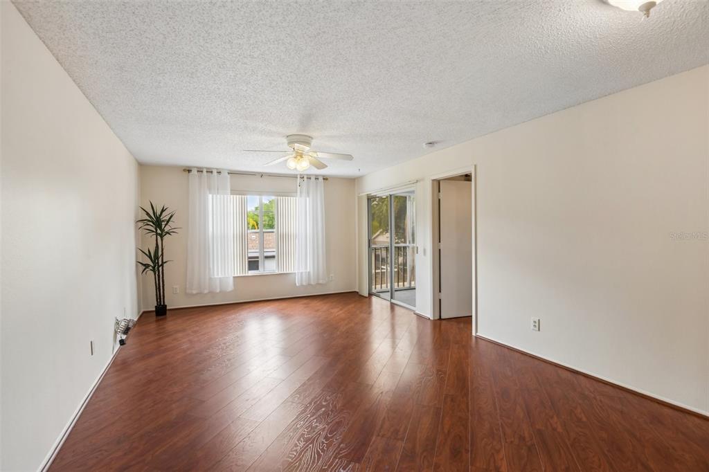 An empty living room features wood-look flooring, a ceiling fan, and a sliding glass door — 7713 HILLSIDE COURT UNIT 204, HUDSON, FL