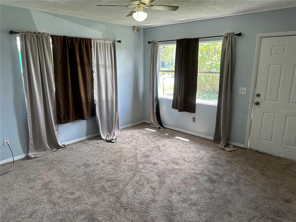 A carpeted living room features light blue walls, two windows with layered curtains, and a ceiling fan — 3715 AVENUE J NW, WINTER HAVEN, FL