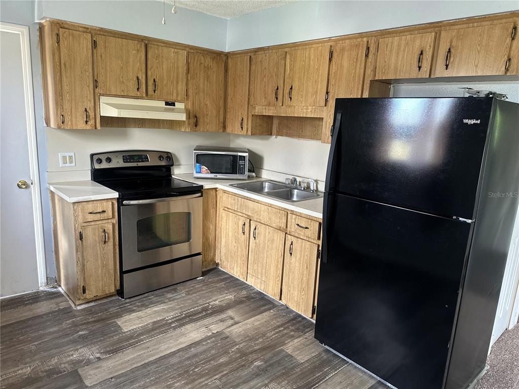 A kitchen features wood cabinets, a stainless steel stove, a black refrigerator, and wood-look flooring — 3715 AVENUE J NW, WINTER HAVEN, FL