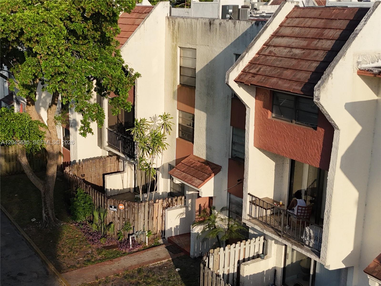 An exterior view of multi-story townhomes with balconies, a wooden fence, and a large tree — 1796 NW 55th Ave # 103, Lauderhill FL 33313, LAUDERHILL, FL