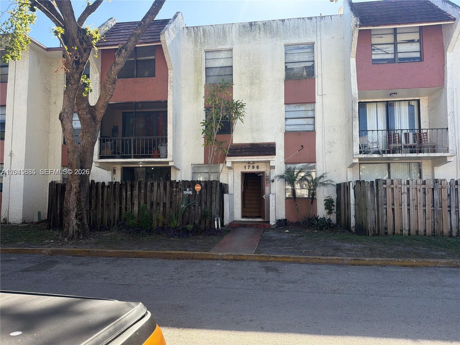 A three-story residential building features white stucco, reddish-brown accents, balconies, and a wooden fence — 1796 NW 55th Ave # 103, Lauderhill FL 33313, LAUDERHILL, FL