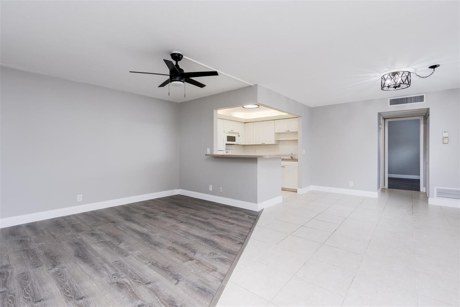 A living room with wood-look flooring and tile features a ceiling fan and kitchen pass-through — 346 Monaco H # 346, Delray Beach FL 33446, DELRAY BEACH, FL