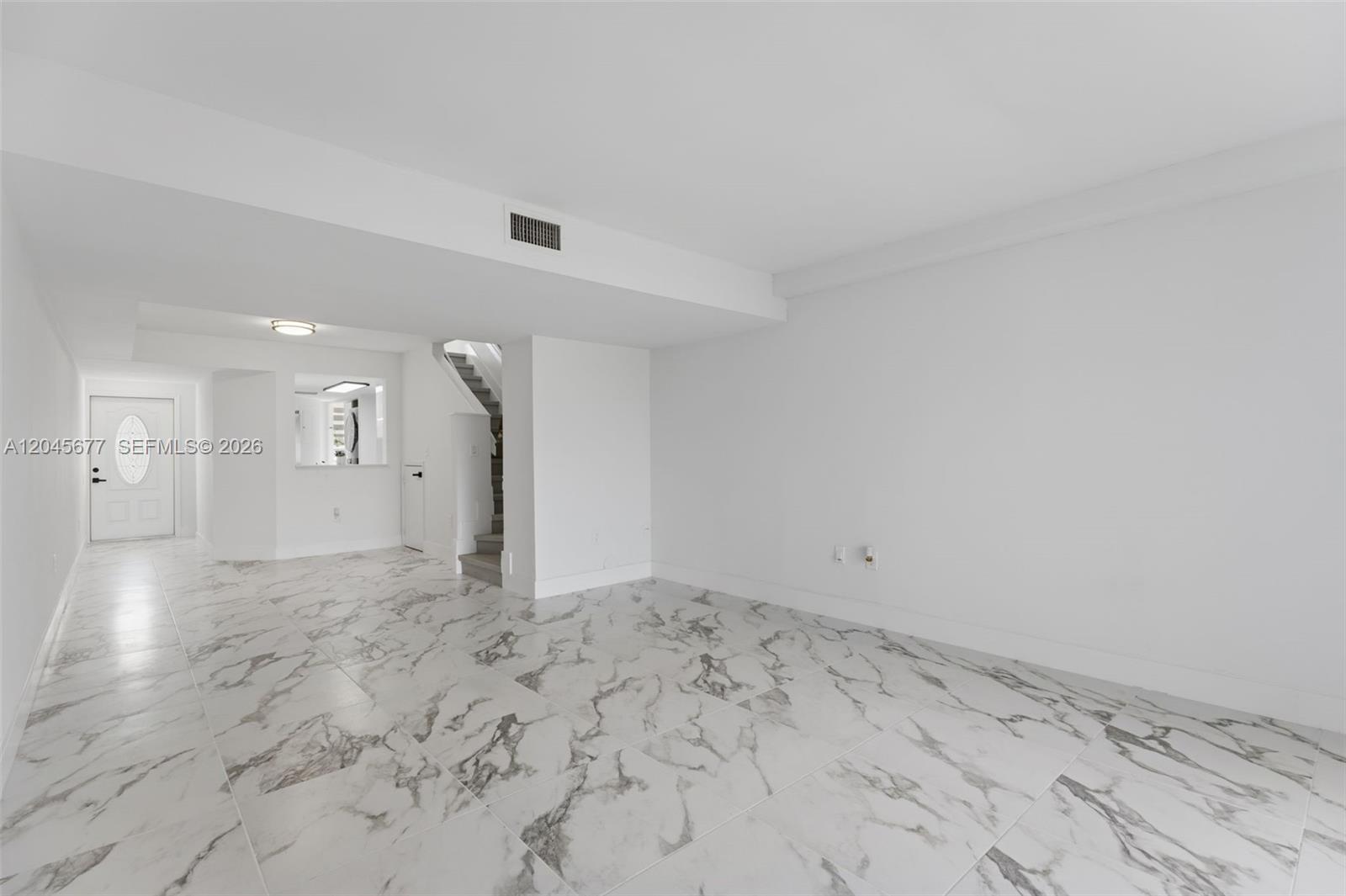 An empty room features white walls, marble-patterned tile flooring, and a staircase — 1030 NW 123rd Ct # 706, Miami FL 33182, MIAMI, FL