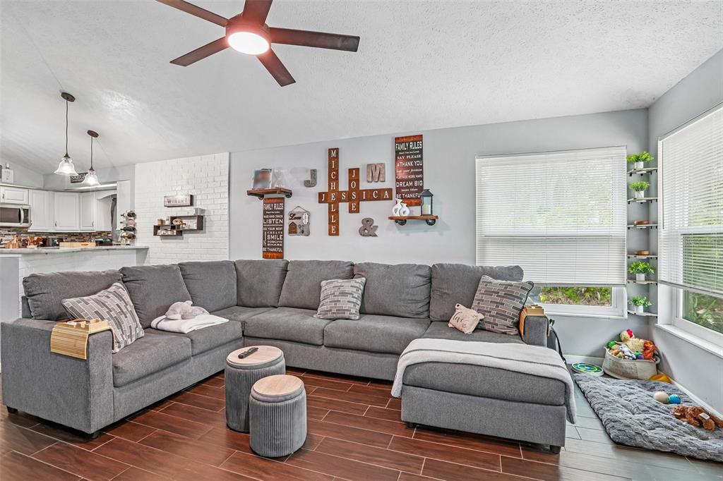 A living room features a large gray sectional sofa, wood-look tile flooring, and wall decor — 4001 BAINWOOD COURT, TAMPA, FL