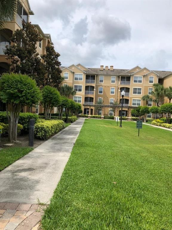 A concrete walkway leads through a grassy courtyard toward a multi-story apartment building — 6466 CAVA ALTA DRIVE UNIT 104, ORLANDO, FL