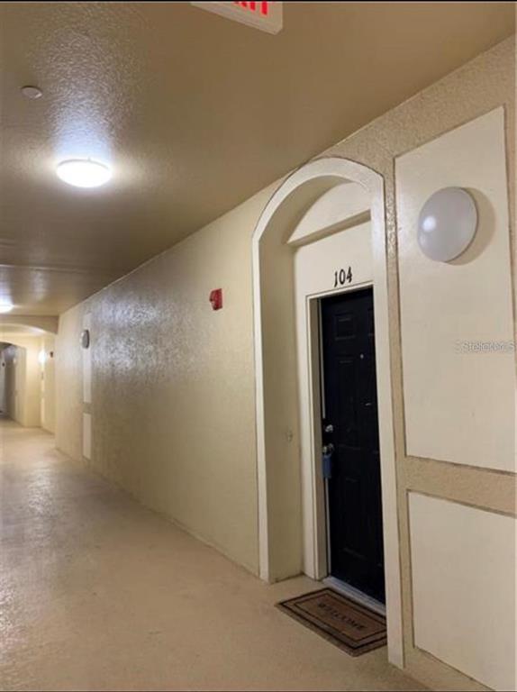 A view of an apartment hallway with a black door labeled 104 and beige walls — 6466 CAVA ALTA DRIVE UNIT 104, ORLANDO, FL