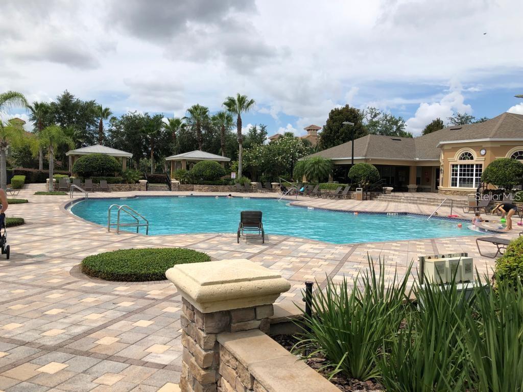 A large outdoor swimming pool with a stone patio and surrounding landscaping — 6466 CAVA ALTA DRIVE UNIT 104, ORLANDO, FL