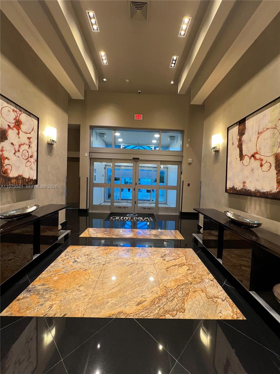 A modern building lobby features a stone floor inlay, dark side tables, and abstract wall art — 3101 S Ocean Dr # 3102, Hollywood FL 33019, HOLLYWOOD, FL