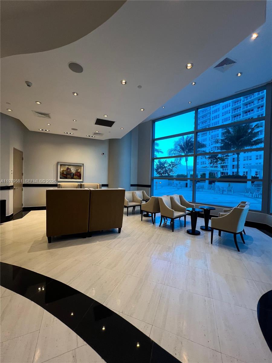 A modern lobby features beige armchairs, floor-to-ceiling windows, and polished light-colored tile flooring — 3101 S Ocean Dr # 3102, Hollywood FL 33019, HOLLYWOOD, FL