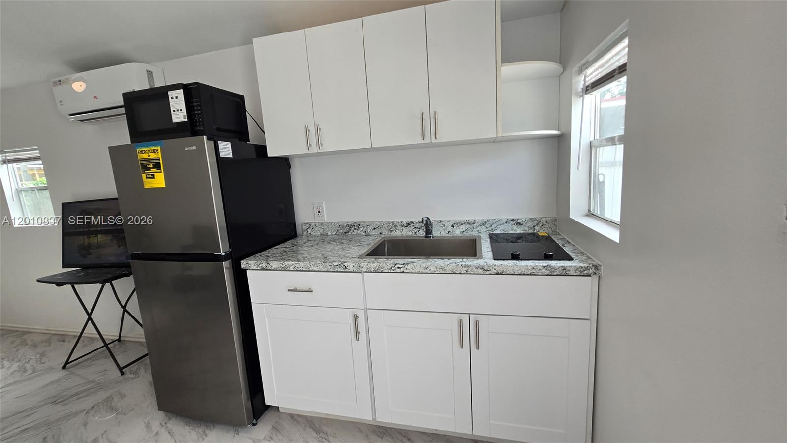 A small kitchen features white cabinets, granite countertops, a stainless steel sink, and a refrigerator — 2440 NW 99th St # A, Miami FL 33147, MIAMI, FL