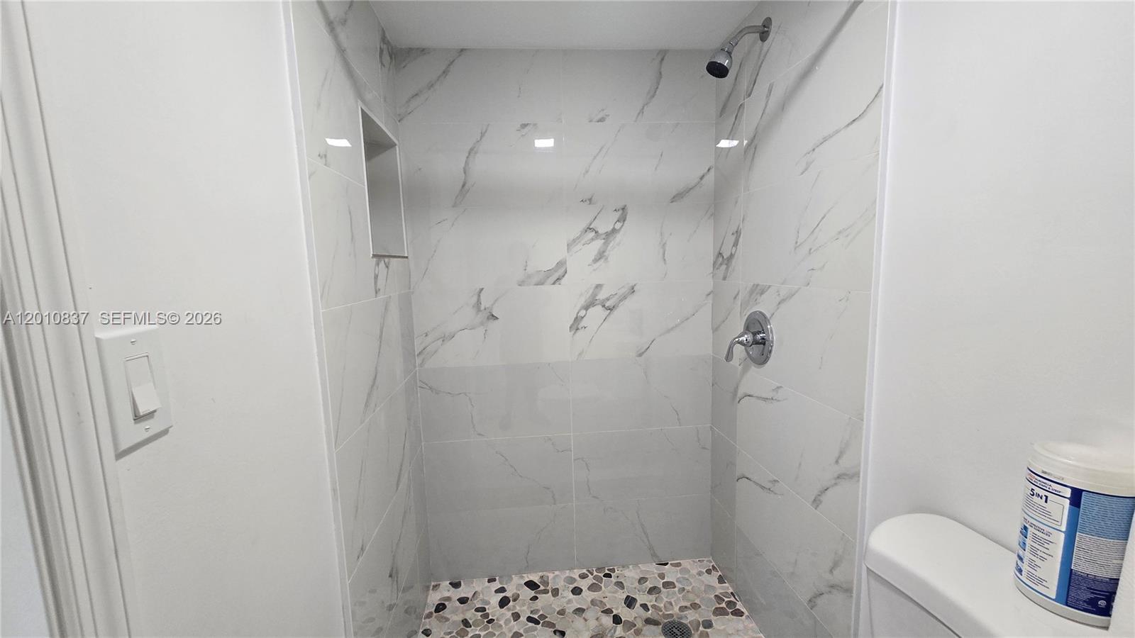 A walk-in shower features white marble-look wall tiles, a pebble floor, and chrome fixtures — 2440 NW 99th St # A, Miami FL 33147, MIAMI, FL