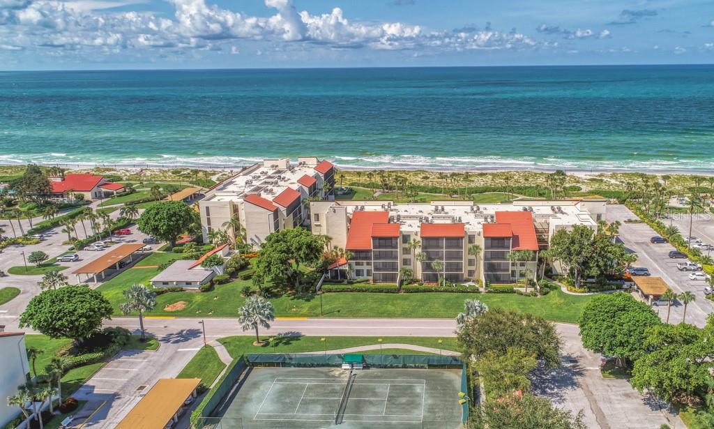 An aerial view shows a beachfront condominium complex with a tennis court and parking lots — 1975 GULF OF MEXICO DRIVE UNIT G4-401, LONGBOAT KEY, FL