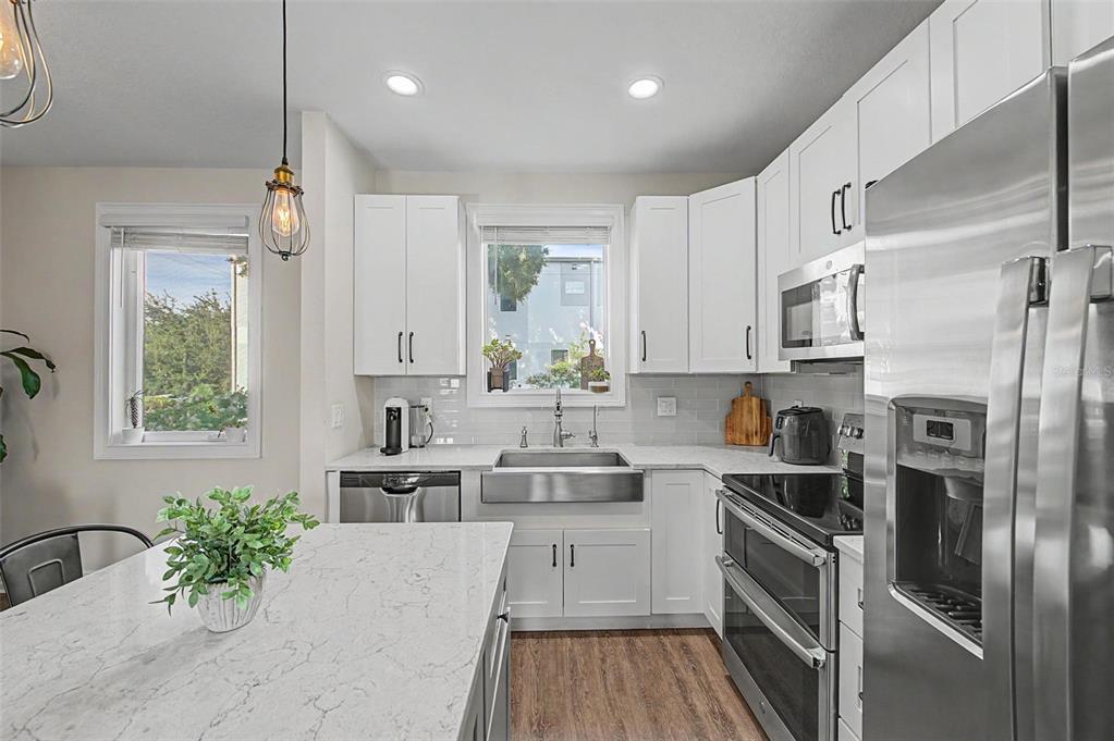 A modern kitchen features white cabinets, stainless steel appliances, a farmhouse sink, and quartz countertops — 1527 N MORGAN STREET, TAMPA, FL