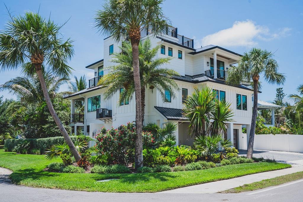 A three-story white house with a rooftop deck, palm trees, and lush landscaping — 526 SEAGULL WAY, ANNA MARIA, FL