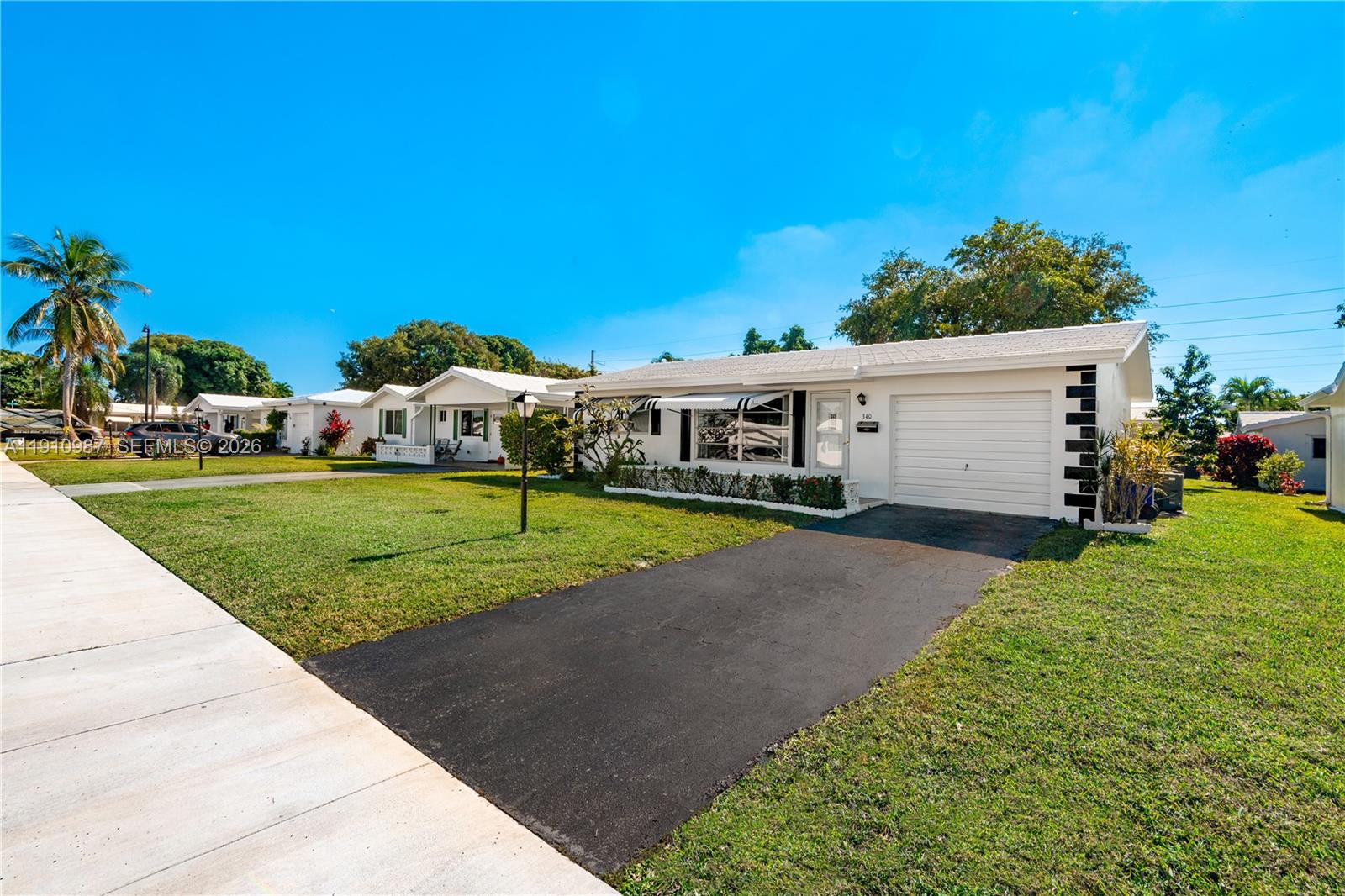 A white single-story house with a garage and a paved driveway sits on a lawn — 340 Leisure Blvd, Pompano Beach FL 33064, POMPANO BEACH, FL