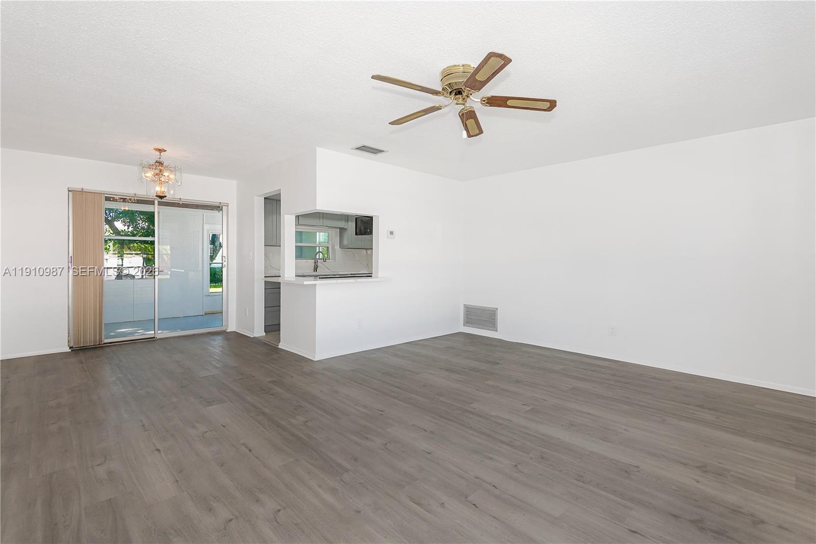 An empty living room features gray wood-look flooring, white walls, a ceiling fan, and a pass-through — 340 Leisure Blvd, Pompano Beach FL 33064, POMPANO BEACH, FL