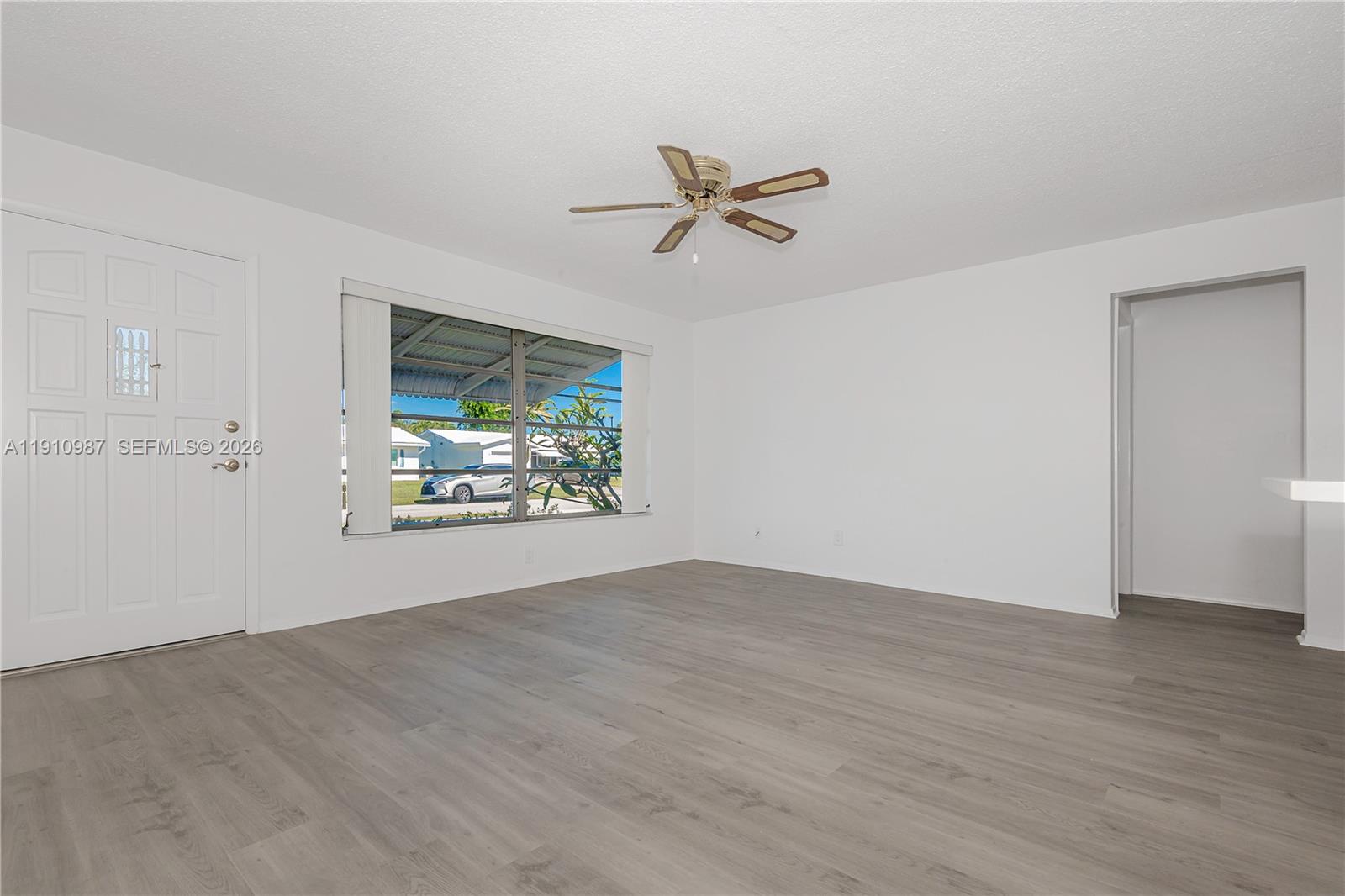 An empty living room features white walls, gray wood-look flooring, and a ceiling fan — 340 Leisure Blvd, Pompano Beach FL 33064, POMPANO BEACH, FL