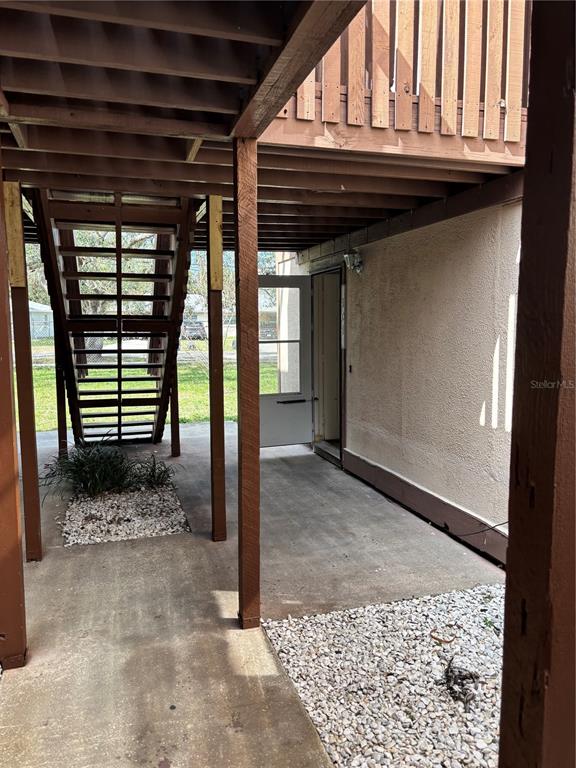 A covered concrete patio area features a wooden staircase and a white exterior door — 5026 WATER OAK DRIVE UNIT 104, BRADENTON, FL