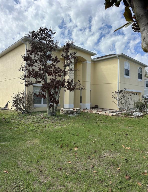 A two-story, yellow stucco house features a front yard with a tree and stone landscaping — 418 MARLBERRY LEAF COURT, KISSIMMEE, FL