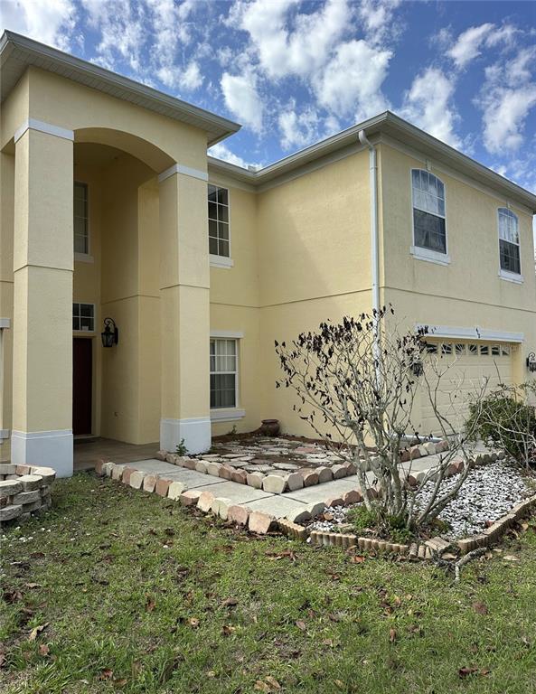 A two-story yellow house features a covered entryway, a garage, and a landscaped front yard — 418 MARLBERRY LEAF COURT, KISSIMMEE, FL