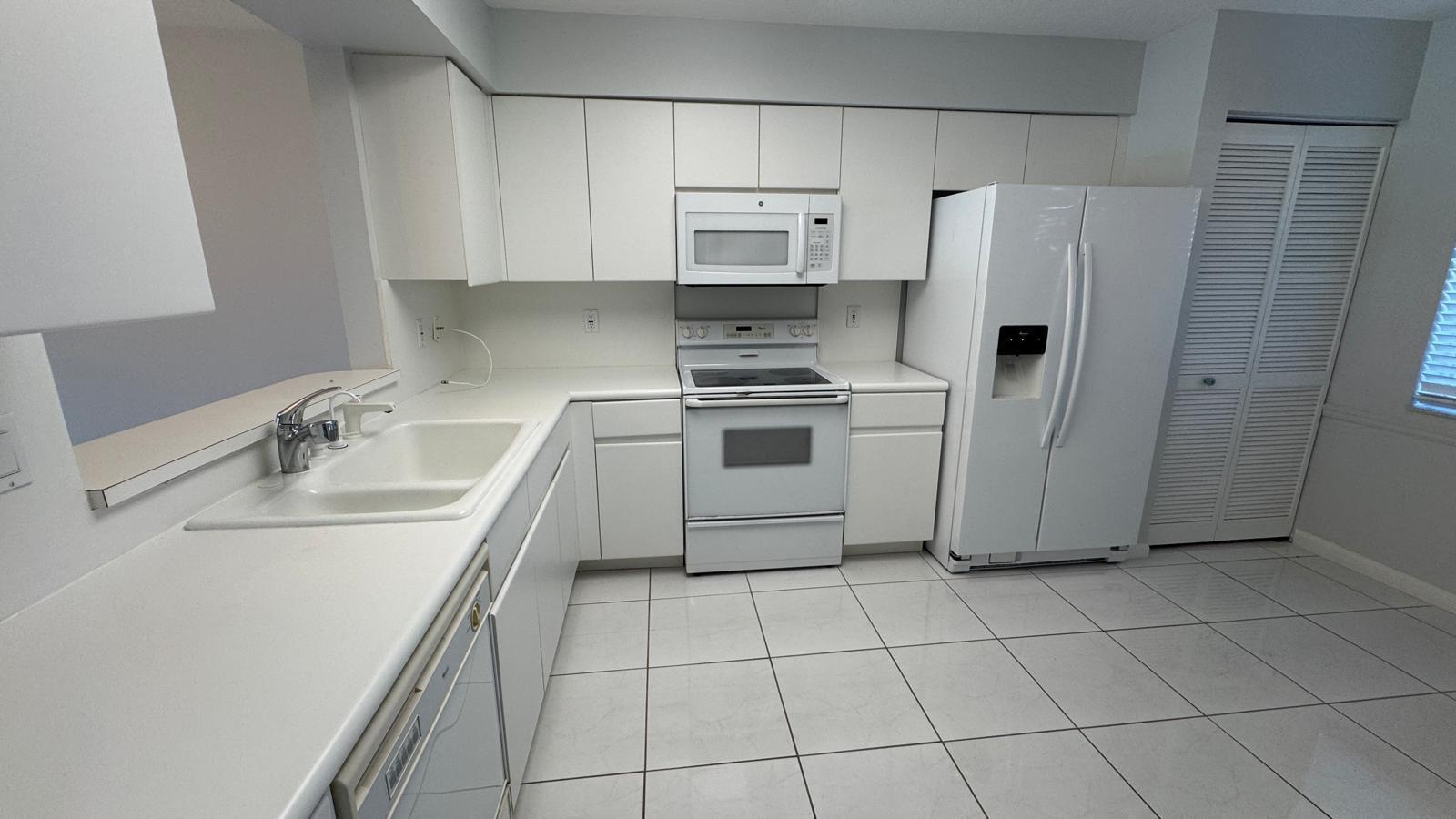 A kitchen with white cabinets, white appliances, a double sink, and light-colored tile flooring — 5876 Regal Glen Drive # 108, Boynton Beach FL 33437, BOYNTON BEACH, FL