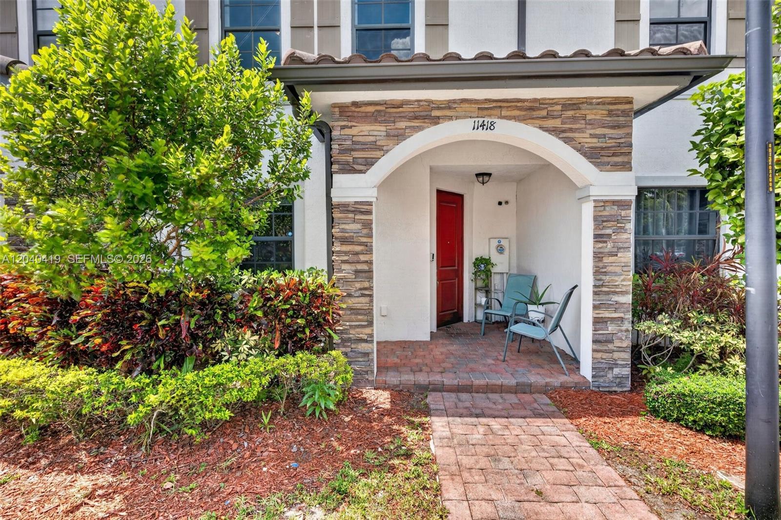 A brick walkway leads to a covered entryway with stone pillars and a red door — 11418 SW 250th St, Homestead FL 33032, HOMESTEAD, FL