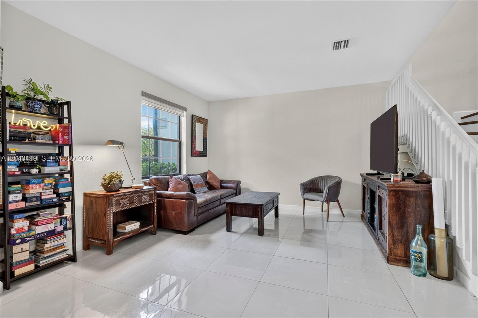 A living room features a brown leather sofa, a television, and a tall bookshelf — 11418 SW 250th St, Homestead FL 33032, HOMESTEAD, FL