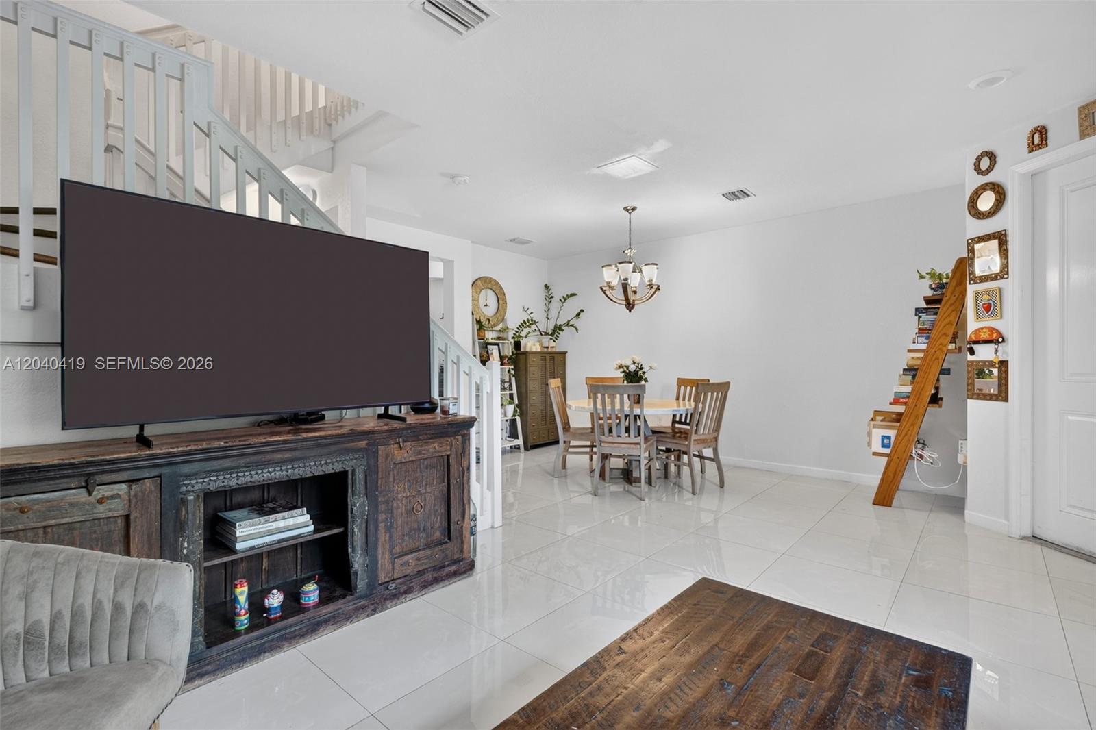 A living and dining area features white tile floors, a wooden media console, and stairs — 11418 SW 250th St, Homestead FL 33032, HOMESTEAD, FL