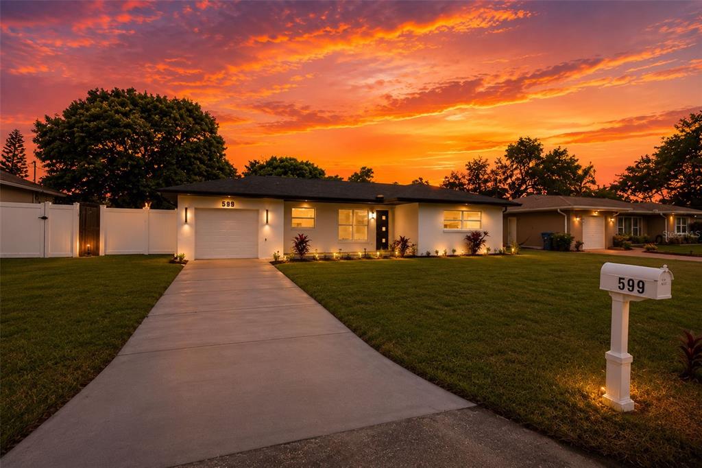 A single-story house with a white exterior, concrete driveway, and lawn at sunset — 599 WOODLAND DRIVE, LARGO, FL