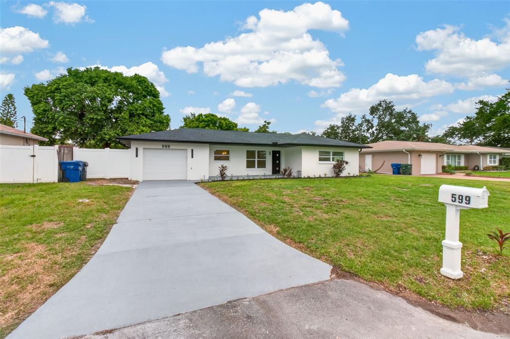 A single-story white house with a dark roof, a concrete driveway, and a front lawn — 599 WOODLAND DRIVE, LARGO, FL