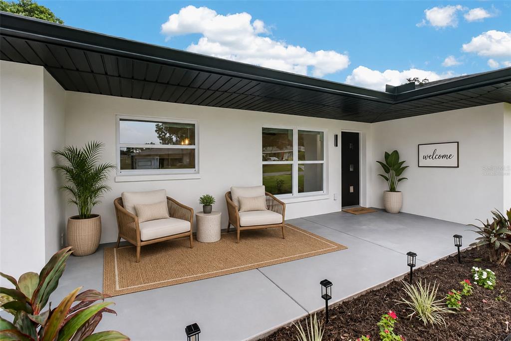 A modern patio features two wicker chairs, a rug, and potted plants under a roof — 599 WOODLAND DRIVE, LARGO, FL