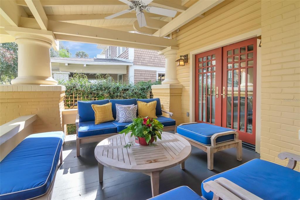 A covered porch features blue cushioned seating, a round wooden coffee table, and red doors — 713 S DELAWARE AVENUE, TAMPA, FL