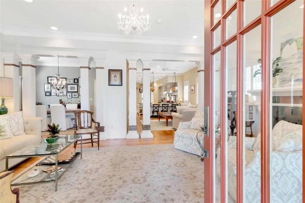 A view through a red-framed door into a living room with white columns and chandeliers — 713 S DELAWARE AVENUE, TAMPA, FL