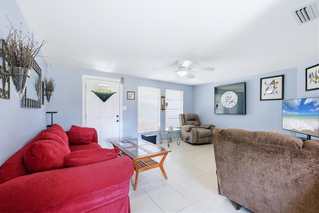 A living room features light blue walls, tile flooring, a recliner, and a television console — 18461 BURKHOLDER CIRCLE, PORT CHARLOTTE, FL